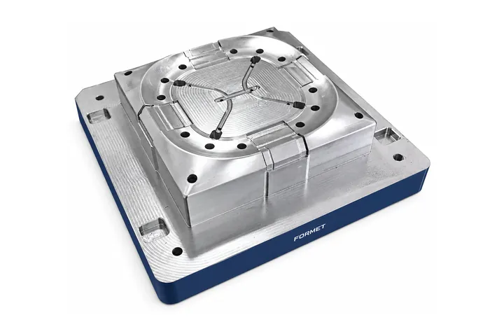 Machined steel mold core with a rounded square cavity on a blue base plate